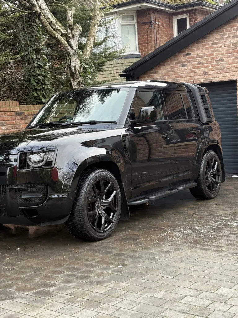 Black Land Rover Defender on a wet driveway