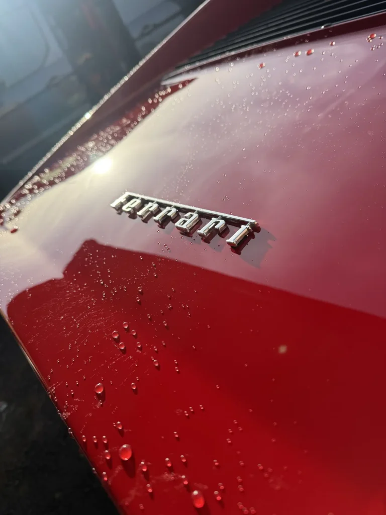 Water droplets on red Ferrari paint beside the Ferrari badge
