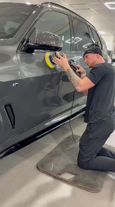 Proshine founder kneeling beside a grey vehicle while machine polishing its side panel