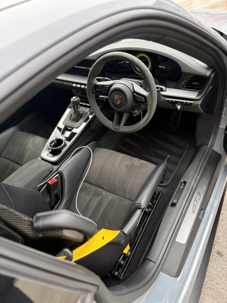 Porsche cabin with dark seats, yellow seat belt and a manual gear lever