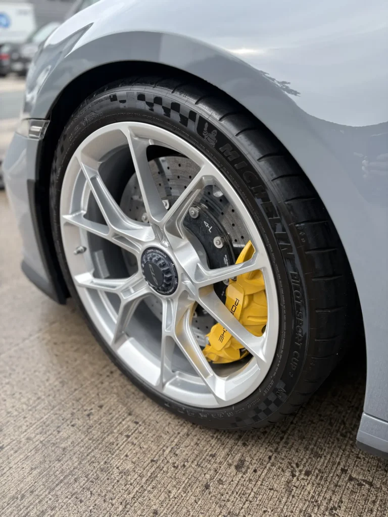 Silver Porsche alloy wheel with yellow brake caliper and drilled brake disc