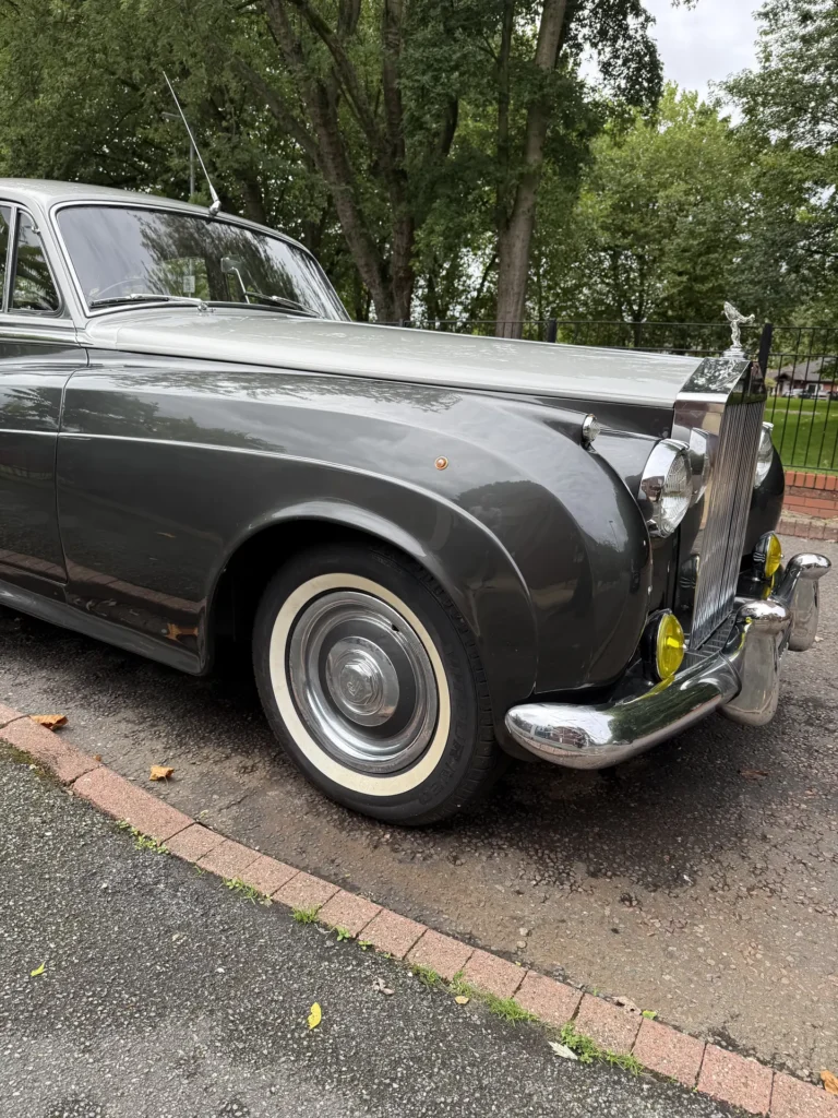 Grey classic Rolls-Royce front wing, chrome grille and wheel beneath trees